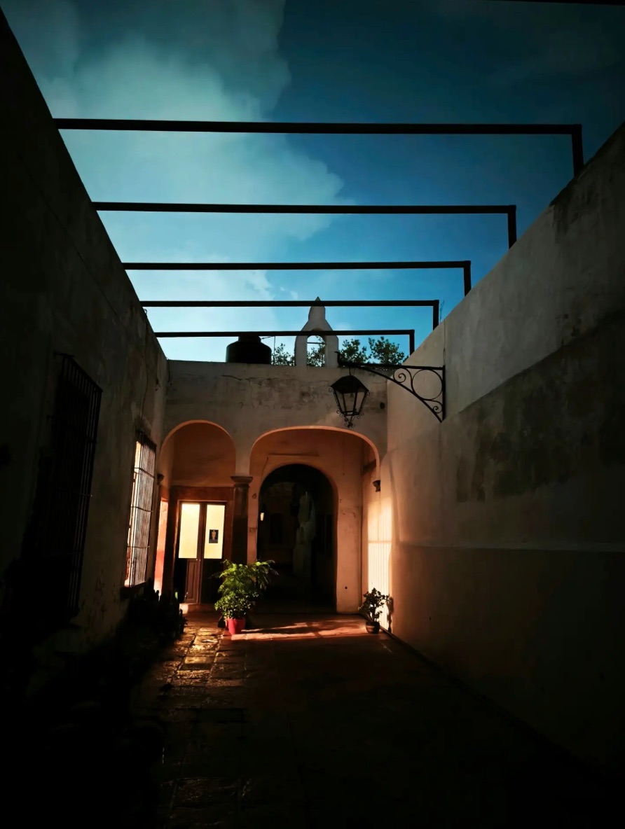Patio de una casa histórica con arcos de cantera y farol de herrería, al atardecer